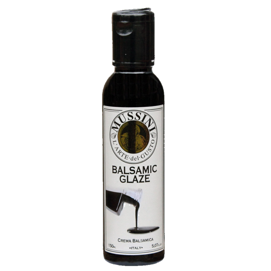 Bottle of Mussini Art & Guest Dark Balsamic Glaze with a label showing the product name and a small cup with a swirl of dark balsamic glaze.