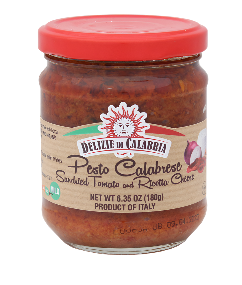 A jar of Pesto Calabrese with a red label, produced by Delizie Di Calabria, showing images of sundried tomatoes and pumpkin seeds, indicating the flavors of the pesto.
